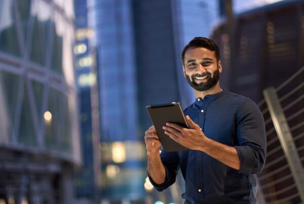 man standing in front of buildings holding a tablet and smiling