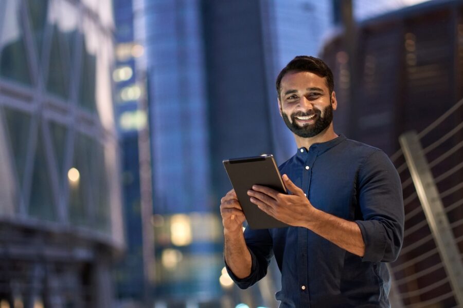 man standing in front of buildings holding a tablet and smiling